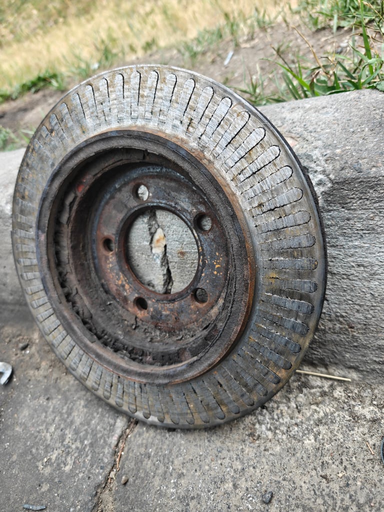 Worn vintage tire with rusted metal wheel rim, lying on concrete surface with grass visible in background