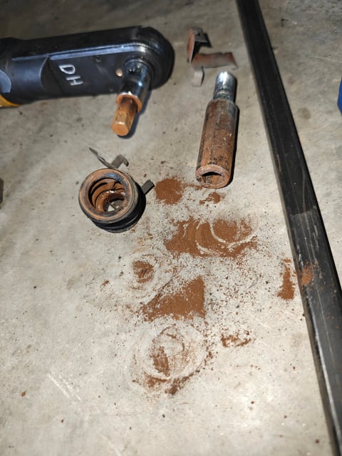 Disassembled rusted vintage pistol parts laid out on concrete surface including barrel, spring, and ammunition