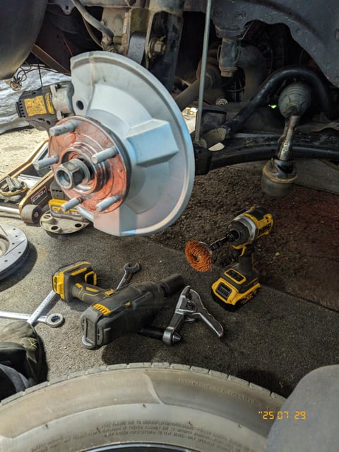 Brake system components during vehicle repair, including rotor, caliper, and yellow power tools on ground